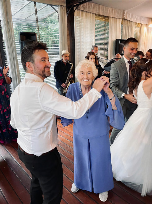 Jay and Grandma dancing with the band behind. Grandma is looking straight into the camera smiling.