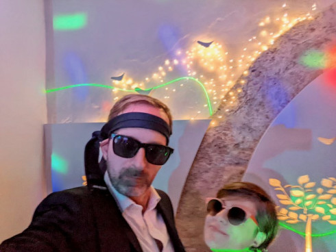 Graham and Anna on the dancefloor with lights behind them. Both are wearing sunglasses and Graham has a tie around his head.