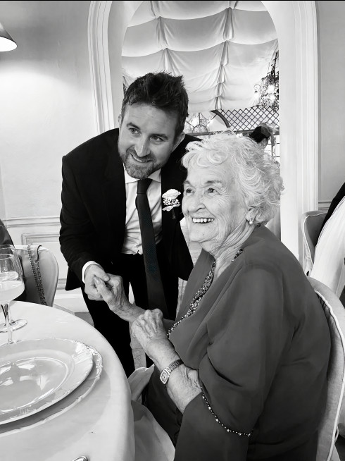 Jay and Grandma at the table holding hands, smiling at the camera.