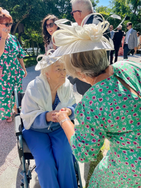 Grandma in a wheelchair in the grounds of the sunny venue surrounded by family.