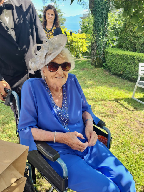 Grandma dressed up in blue with a wedding hat, sat in a wheelchair.