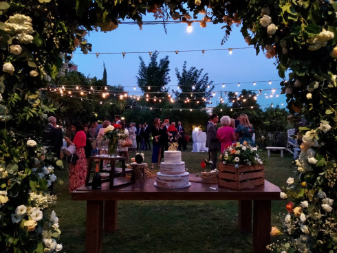 Evening sets with the uncut cake in between the arch and people in the garden beneath fairy lights, chatting.