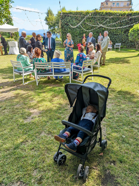 Baby Valentino sleeps in a pushchair with a semi circle of guests talking behind him.