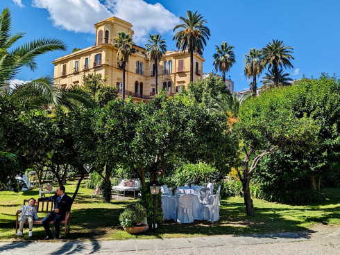The garden grounds with a large sand-coloured villa behind it.