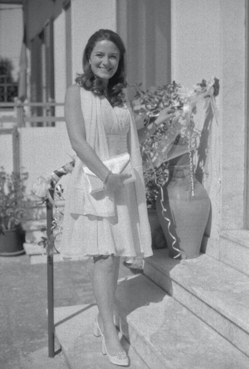 Filly standing on the steps of her home in her civil ceremony dress clutching her handbag smiling.