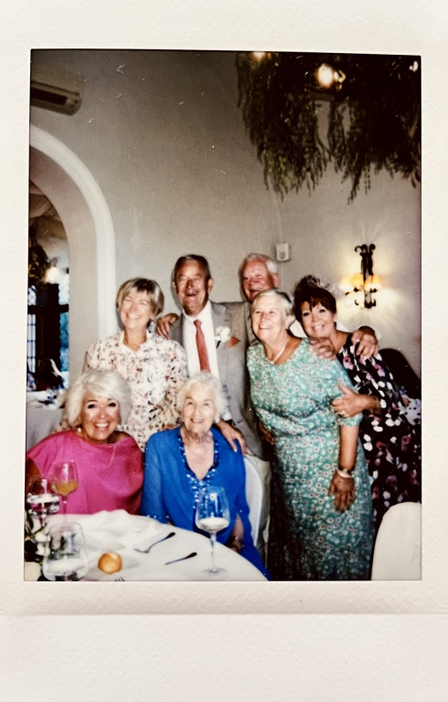 Mum and Grandma at the table, with members of Jay's family behind laughing.