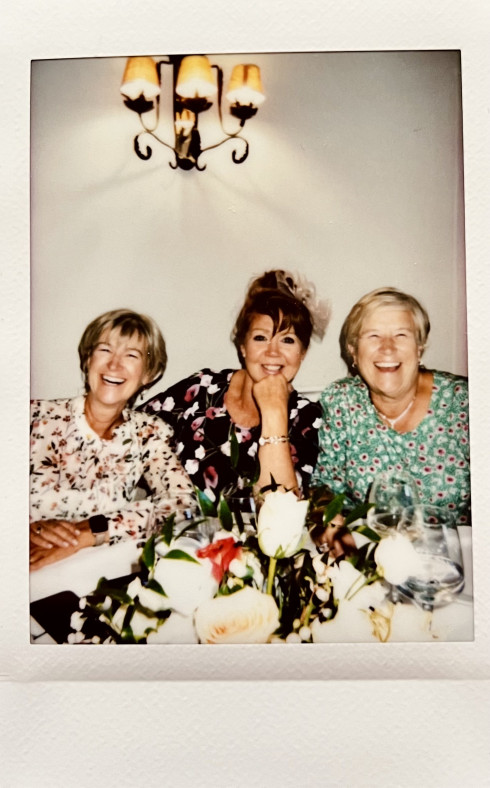 Leanne, Nicola, and Lesley laughing at the table with a flower arrangement in the foreground.